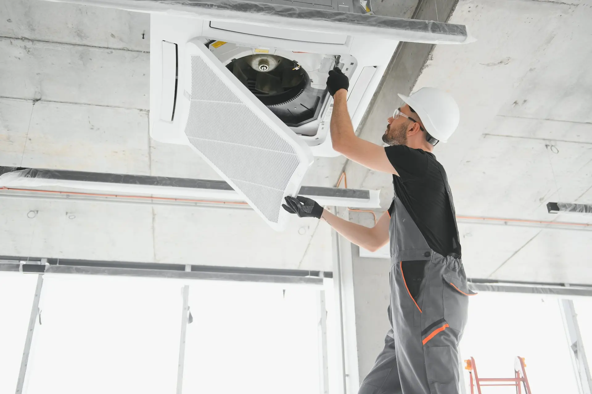 Worker repairing ceiling air conditioning unit.